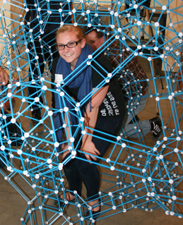 A student crouches in the middle of a large geometric structure.